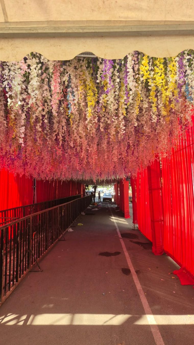 A covered walkway with red cloth along the sides and a ceiling full of hanging artificial flowers in white, pink, purple and yellow