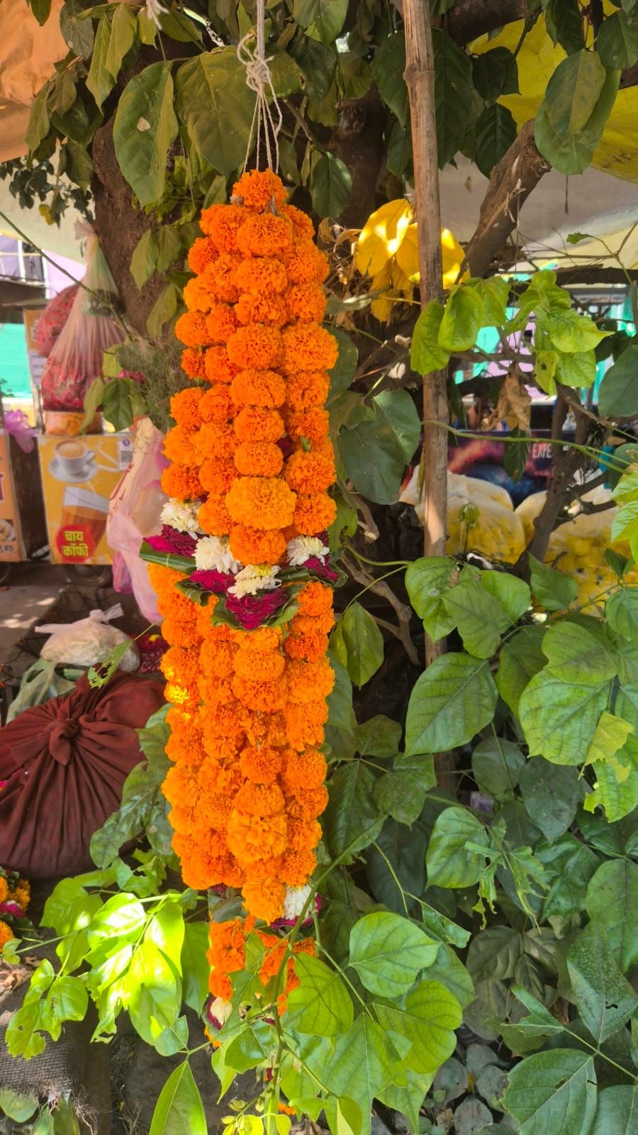 A long garland of orange marigolds with small white and red flowers, hanging from a tree at a flower stall